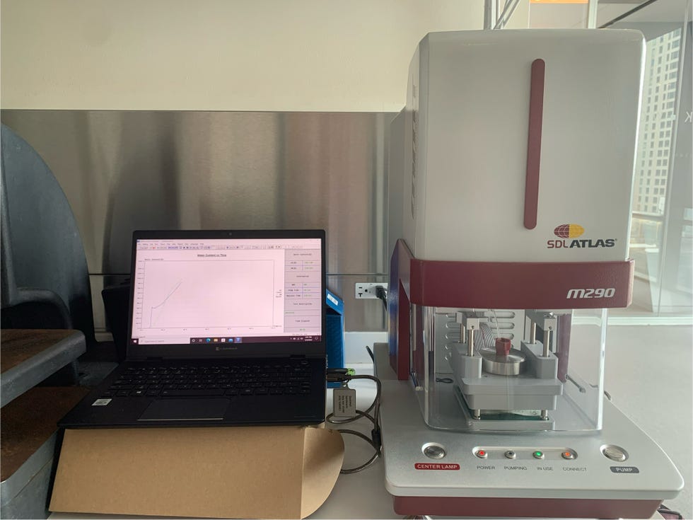 a moisture management tester in red and gray next to a black laptop recording fabric response and wicking speed to a sweat solution
