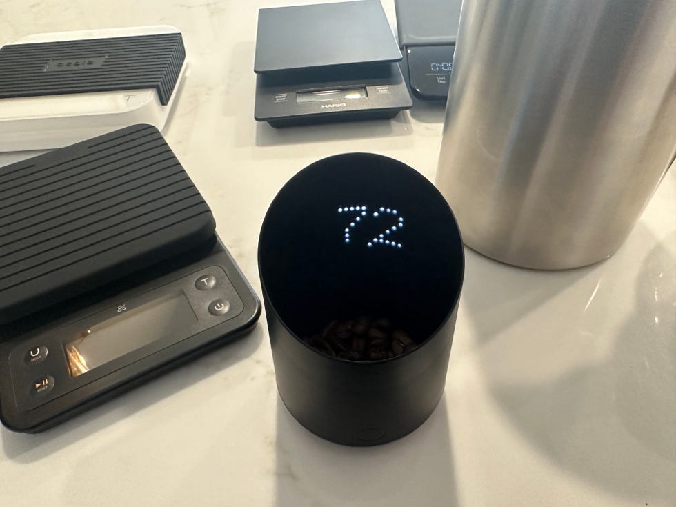 coffee scale with coffee beans inside and other scales around it on a marble countertop