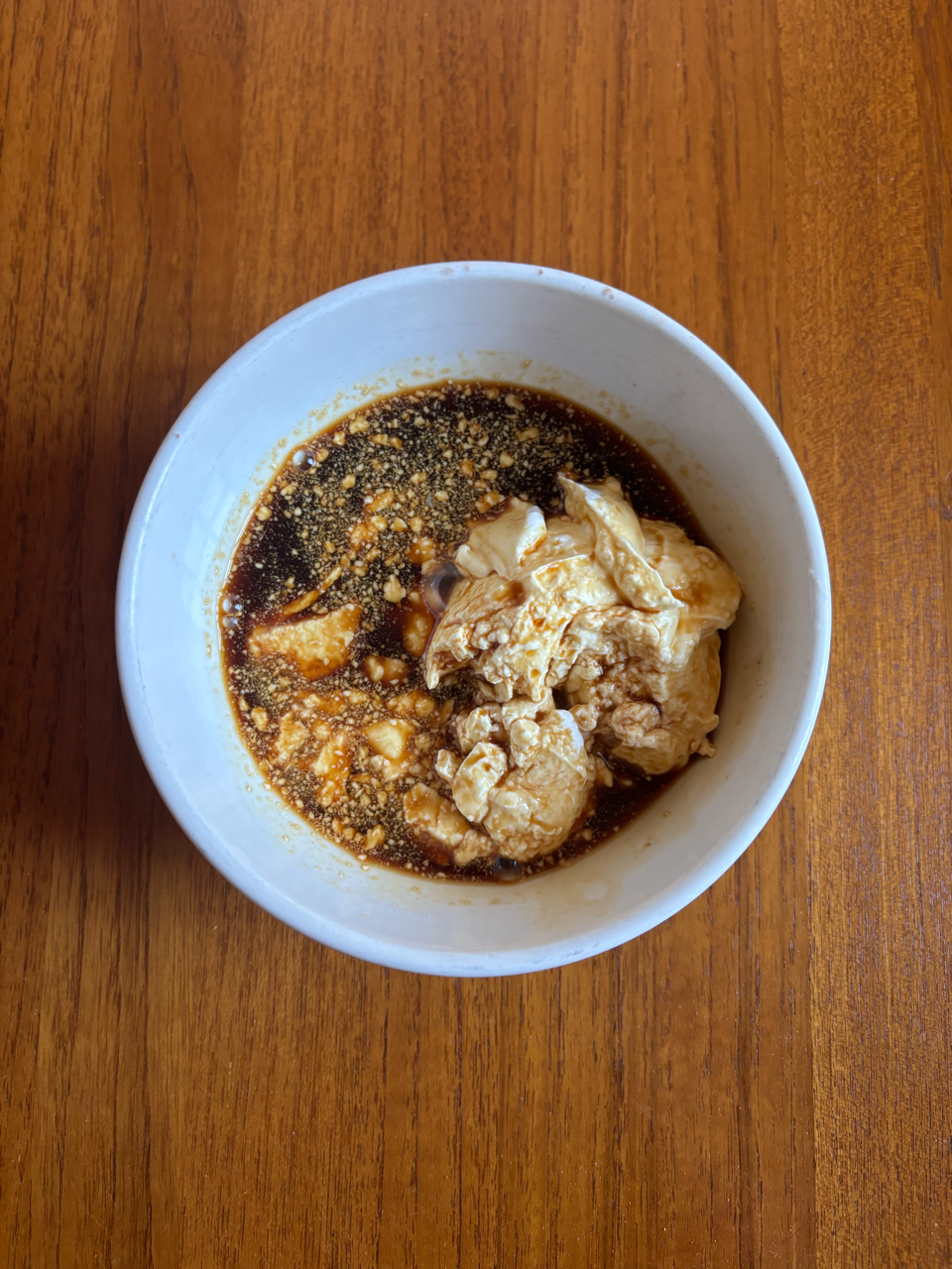 bowl containing a mixture of soft tofu in a dark sauce with a sprinkle of spices on top