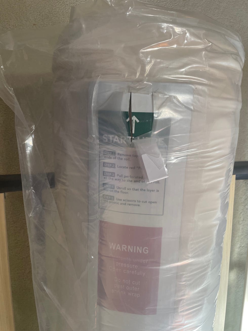 a rolled up compressed mattress sealed in plastic with a pull out tab