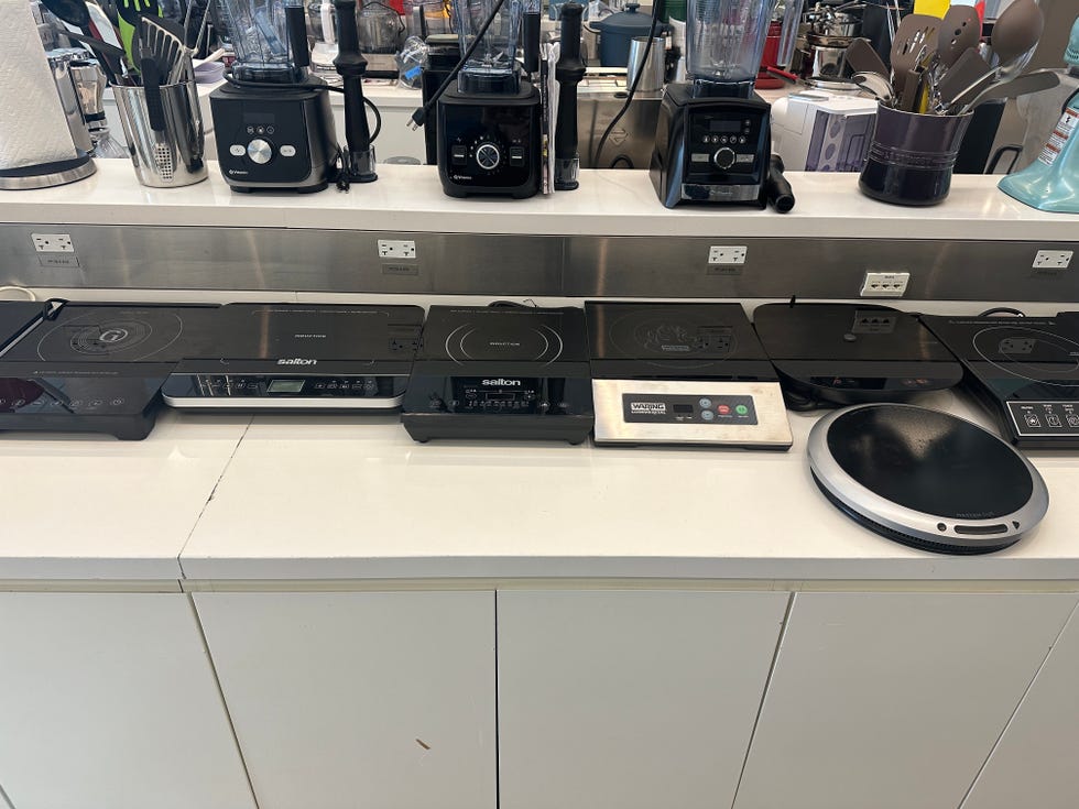 a line of induction cooktops and blenders on a kitchen countertop