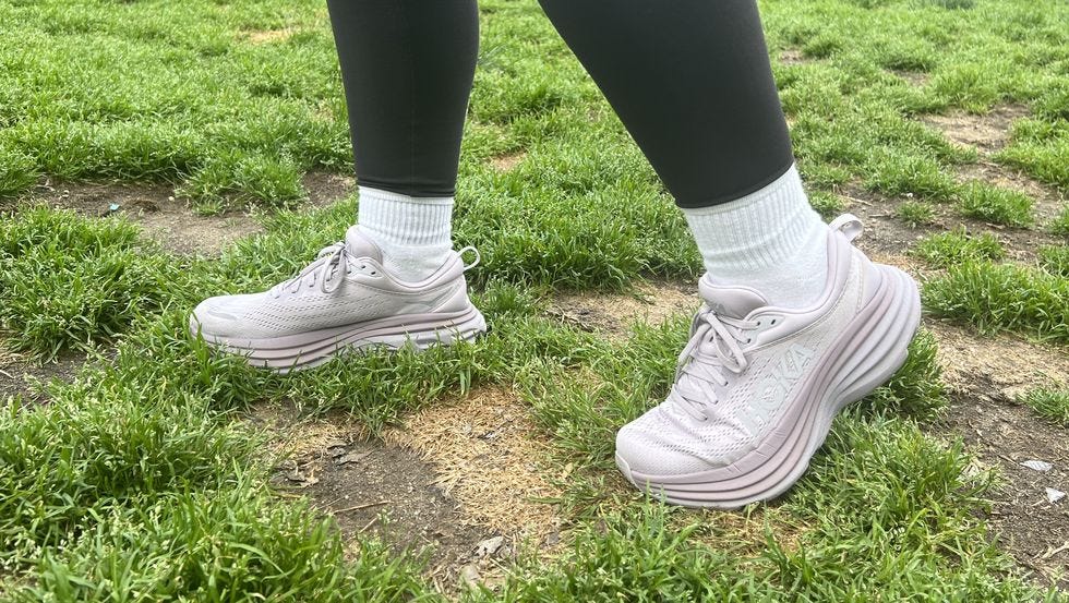 a person's feet in white sneakers from hoka on grass