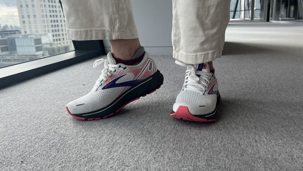 a pair of feet wearing white, black and red sneakers from brooks against grey carpeting