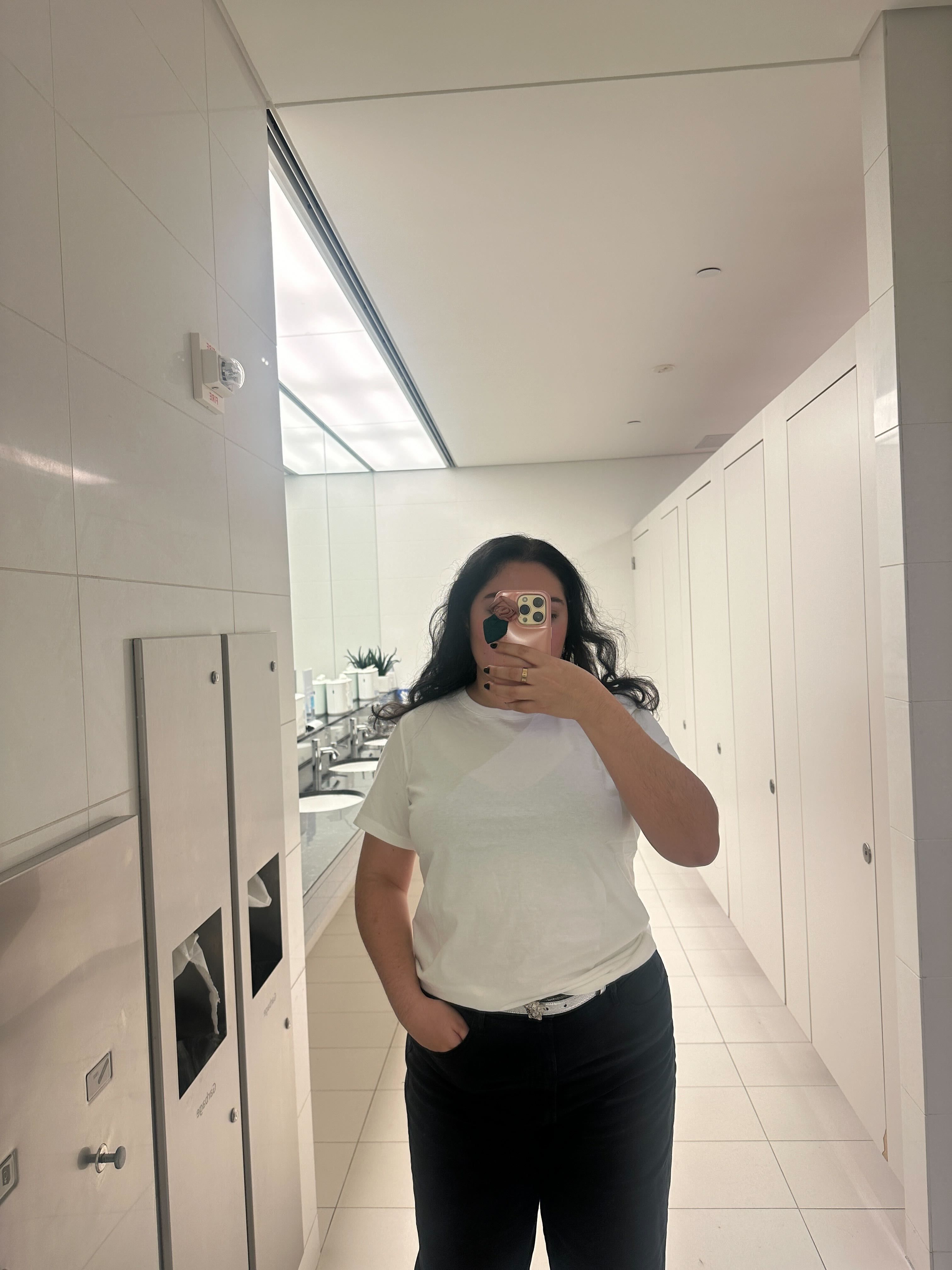 person wearing a white tshirt in a bathroom with mirrors and stalls