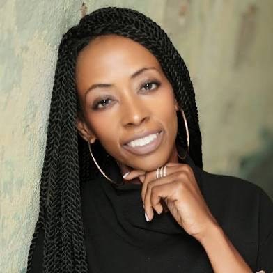 a person with braided hair and a black top poses against a textured wall