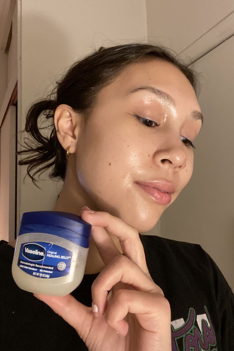 an image of jacqueline saguin, associate editor of products and reviews at good housekeeping holding a blue bottle of vaseline original healing jelly to slug her face
