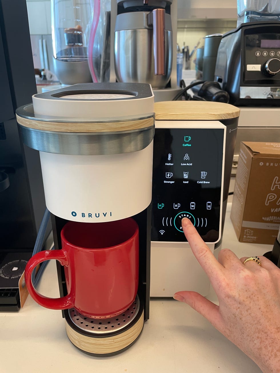 hand pressing start button on bruvi single serve coffee maker