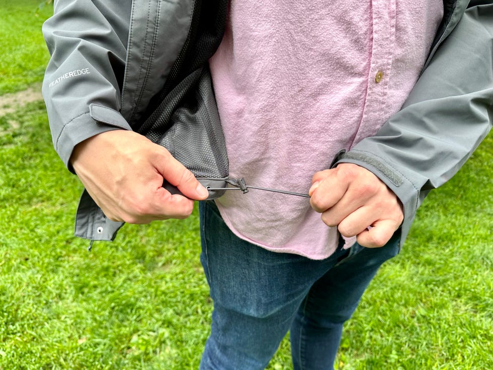 a person pulling the hem drawcord on a grey eddie bauer rain jacket