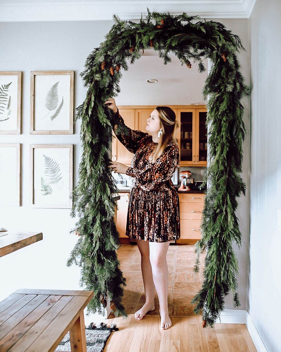 a woman hangs a holiday garland across a doorway
