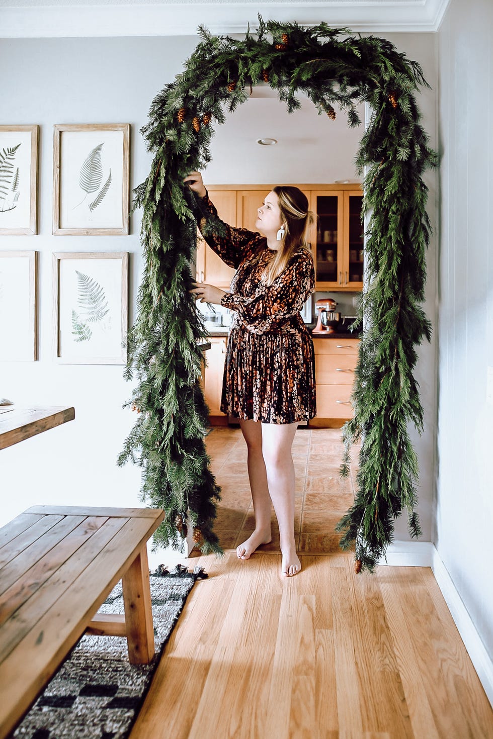 a woman hangs a holiday garland across a doorway