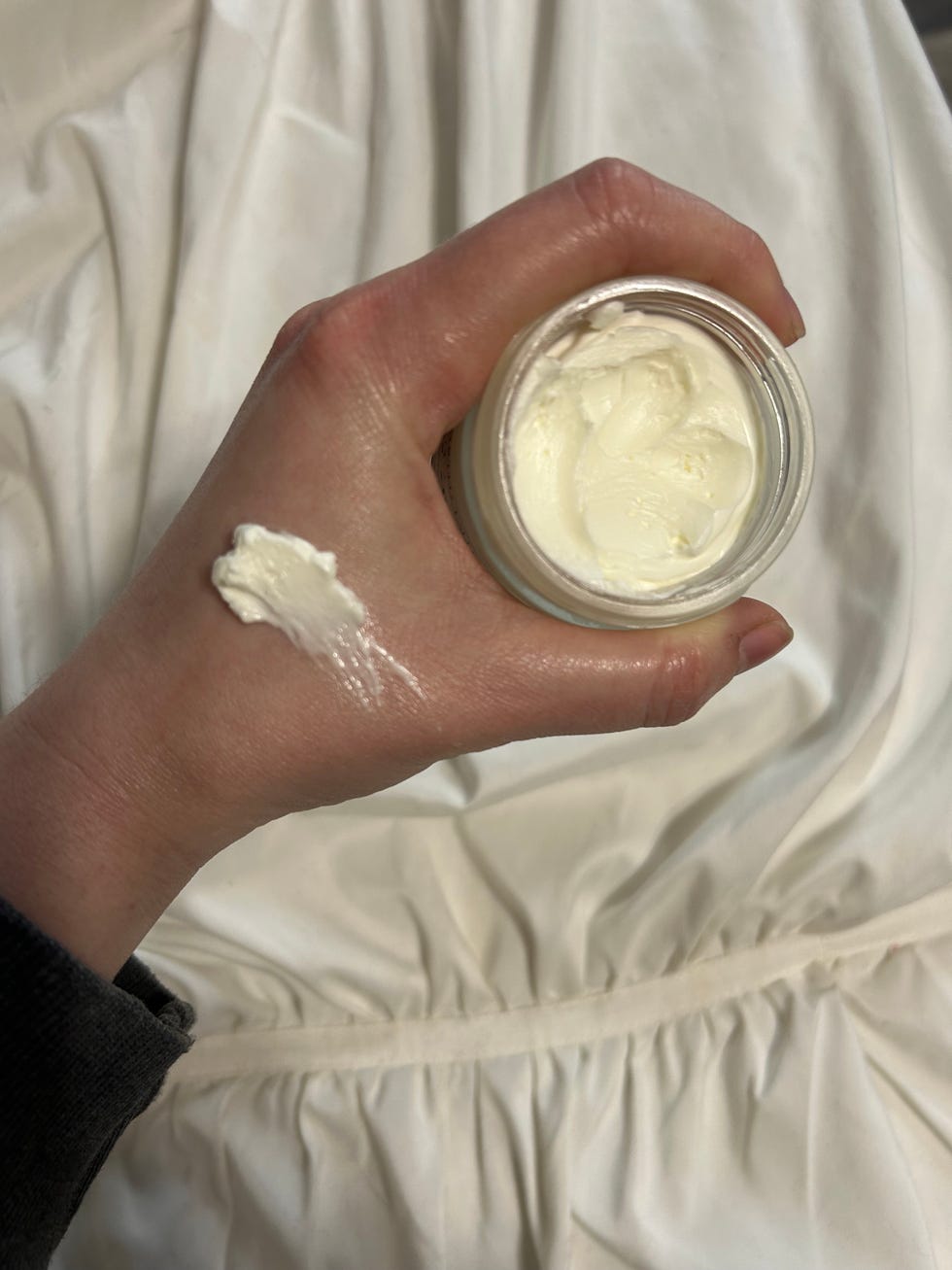 hand holding a jar of cream with a small amount applied on the wrist