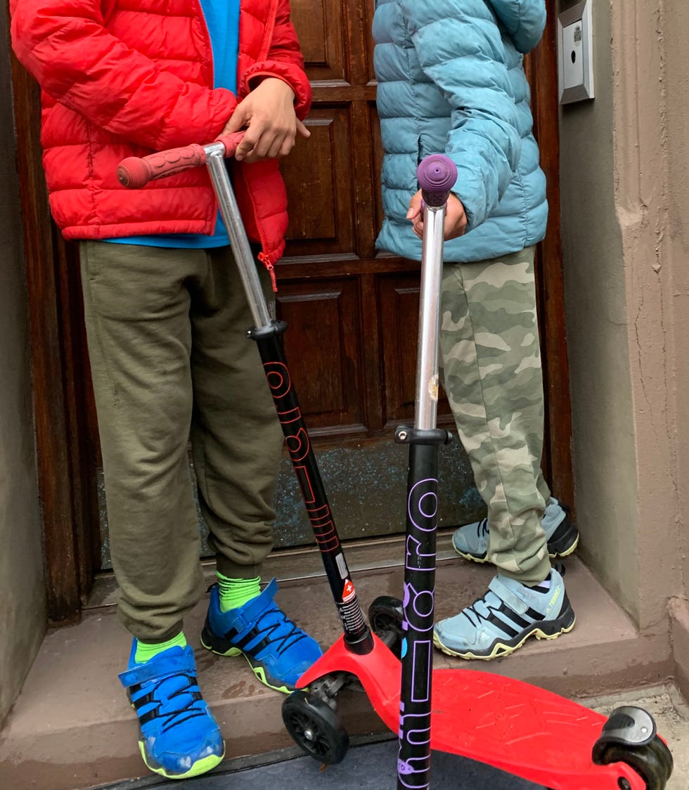 two kids with scooters wear adidas sneakers, a good housekeeping pick for best children's walking shoes