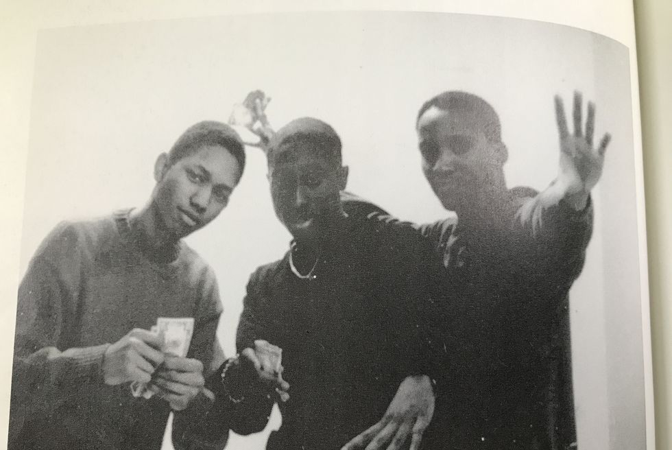 tupac shakur and two friends post for a photo, tupac is in the middle and holds some cash in one hand