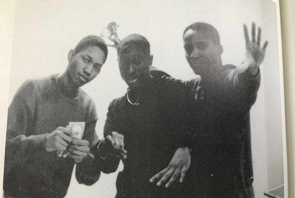 tupac shakur and two friends post for a photo, tupac is in the middle and holds some cash in one hand