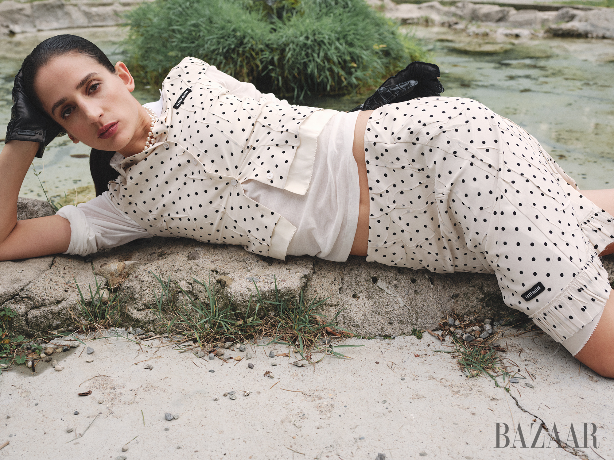 fashion model lying on a rocky surface near water wearing a polkadot outfit