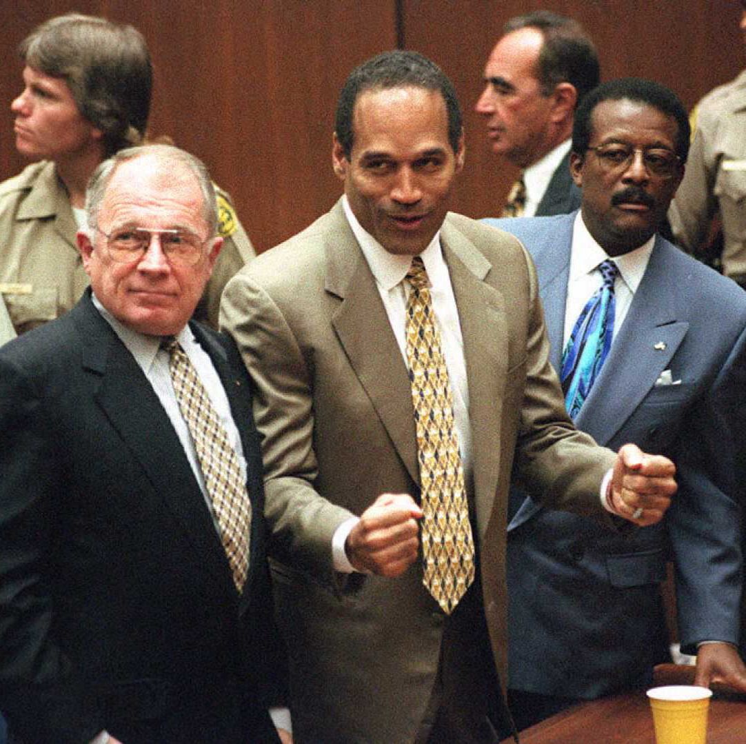 f lee bailey stands and looks left, oj simpson holds his fists in front of him and looks left, johnnie cochran stands and looks left, all three men wear suits with ties