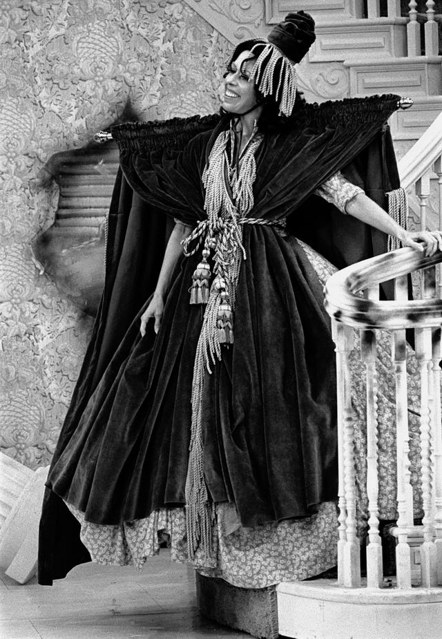 carol burnett wears a curtain rod and curtains and stands on a staircase while smiling during an episode of the carol burnett show