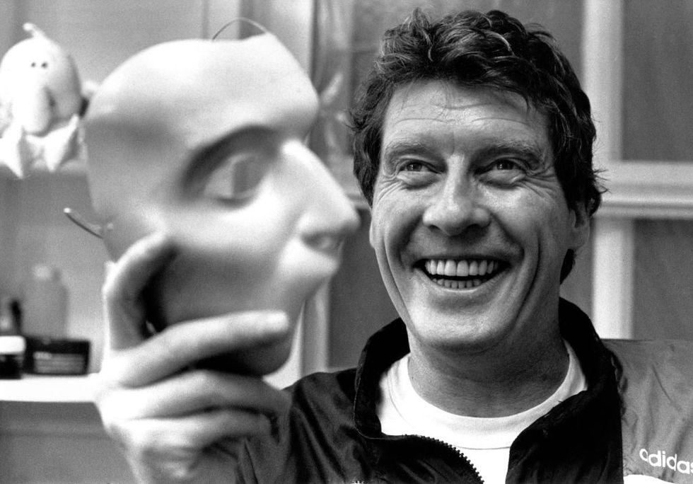 a black and white photo of michael crawford smiling and holding a white face mask in a dressing room
