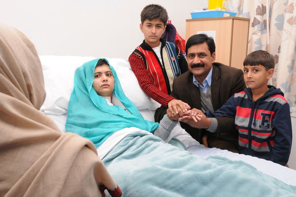malala yousafzai lies in a hospital bed as her father and two younger brothers hold her hand from the side of the bed