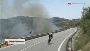 un ciclista pedalea junto a un incendio en la vuelta ciclista a madrid sub23