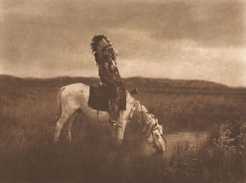 Een lid citizen van de Blackfoot Nation zit op zijn paard terwijl het dier drinkt uit de rivier Bow in Alberta in Canada