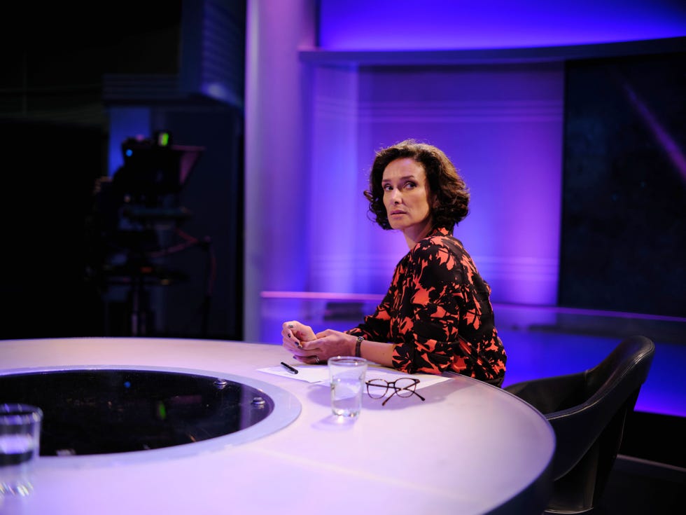a person seated at a round table in a studio with a camera in the background