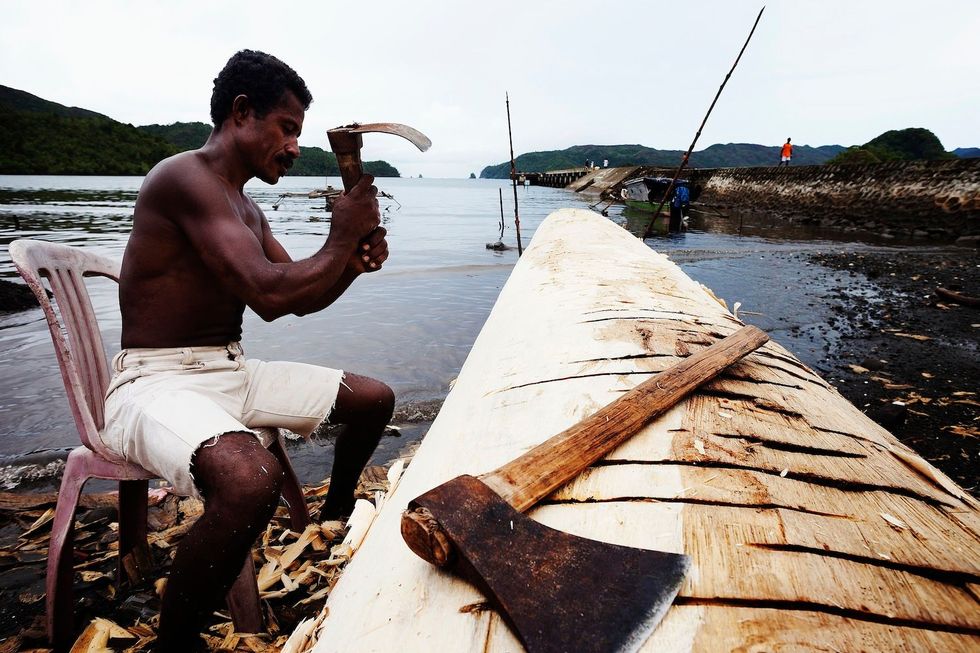 Een visser hakt zijn boot uit een boomstam in een kleine nederzetting op n van de eilanden