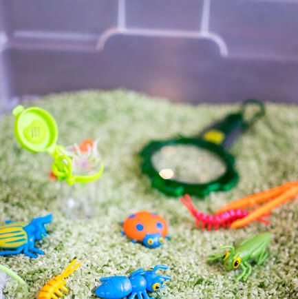 a sensory bin filled with green rice, bug toys, a magnifying glass and other objects