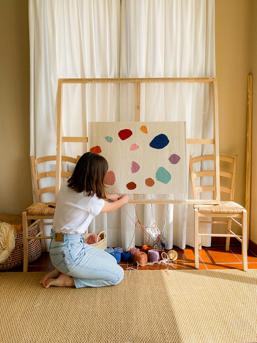 una mujer tejiendo en un telar con un tapiz de colores