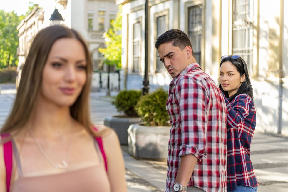 infidelity concept unfaithful womanizer guy turning around amazed at another woman while walking with his girlfriend on street