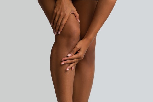 trauma, stretching. cropped of afro woman massaging her sore injured knee, grey background