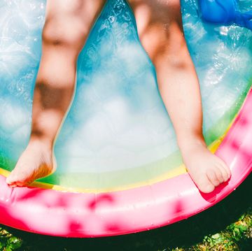 childs legs in colorful inflatable pool on grass surrounded by pool toys