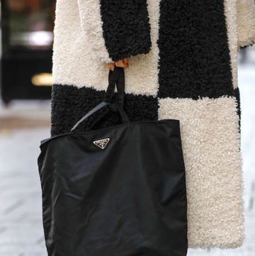 a woman carrying a black prada nylon tote bag wearing a black and ivory checkerboard shearling coat on the street in duesseldorf