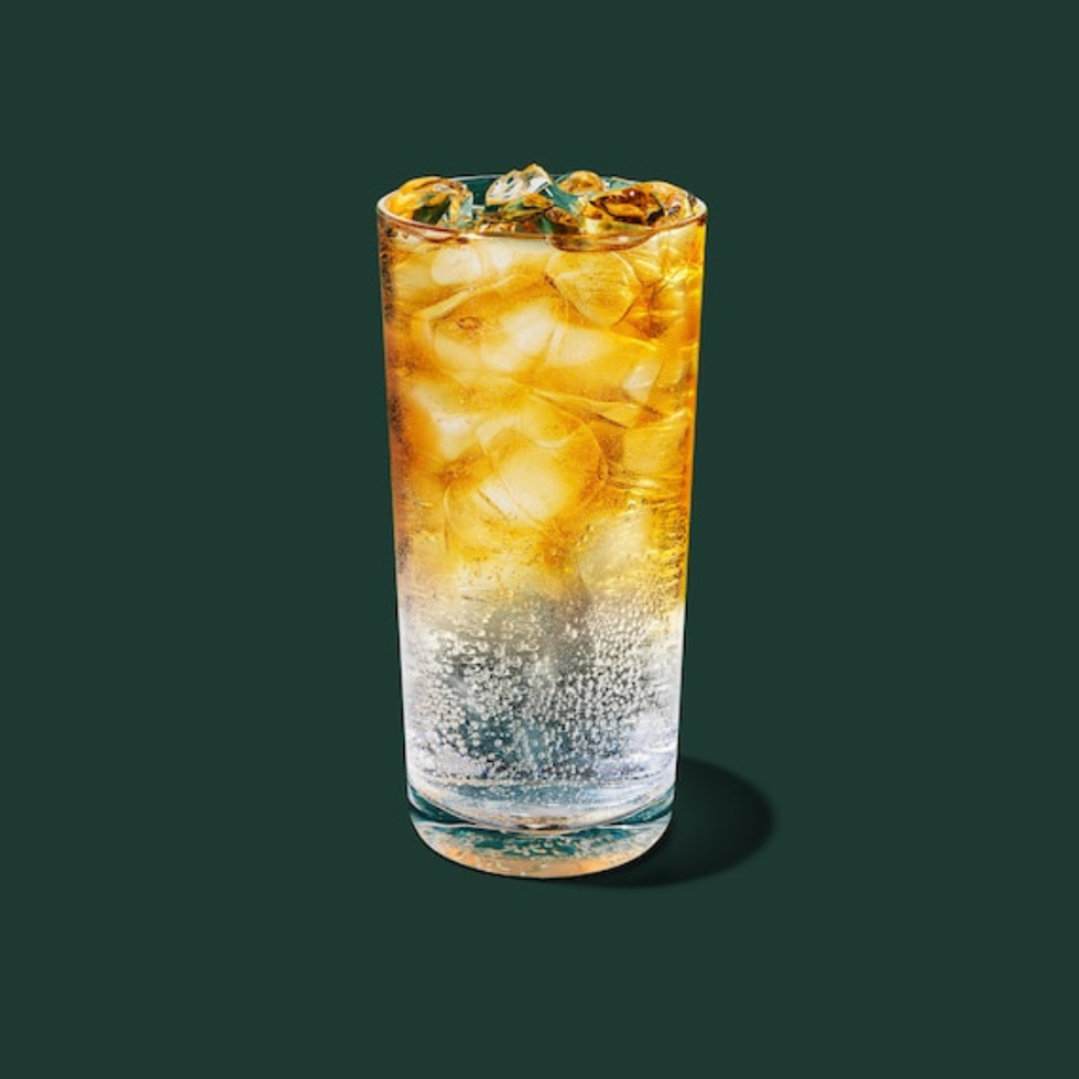 a tall glass containing a fizzy beverage with ice and a golden hue