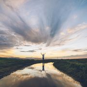 inspirational bible verses person standing near a meadow and river and holding up their arms to the sky