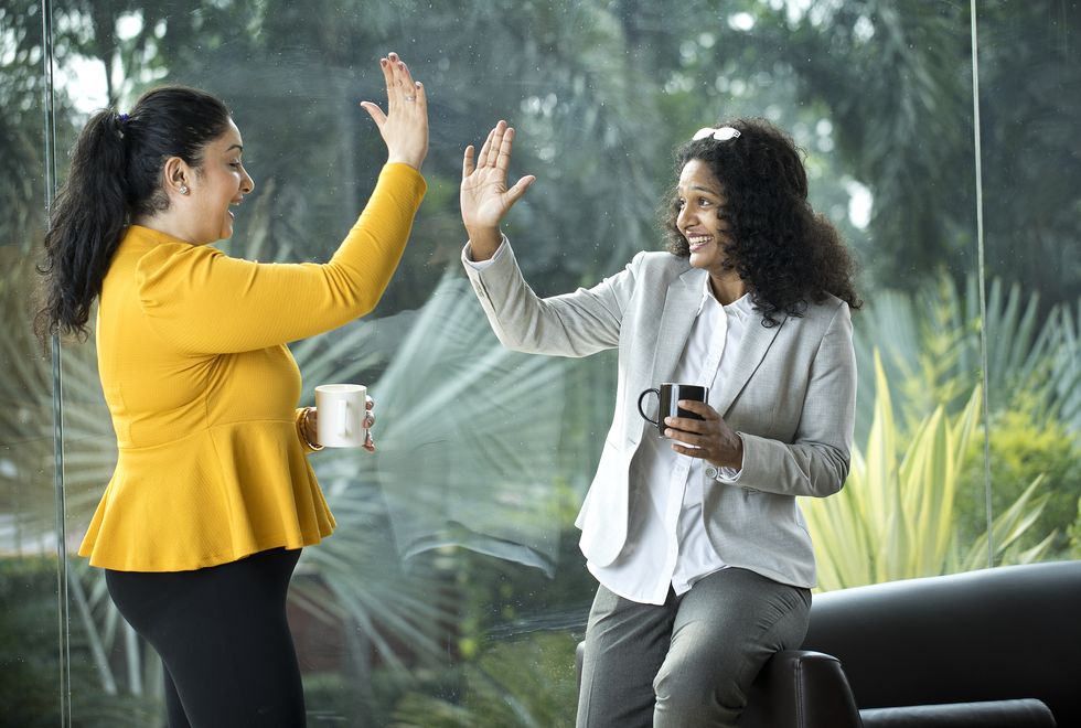 two happy businesswomen celebrating success by giving high five to each other at office