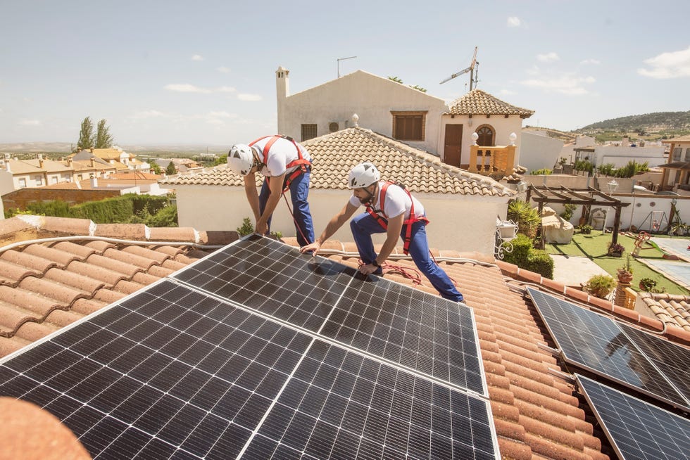 dos obreros instalan placas solares en una casa