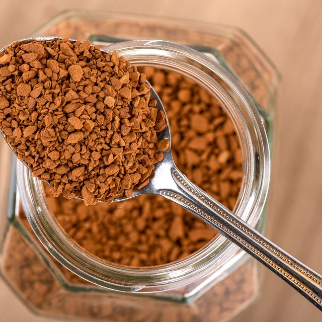 instant granulated coffee in a spoon over a jar on a wooden background.