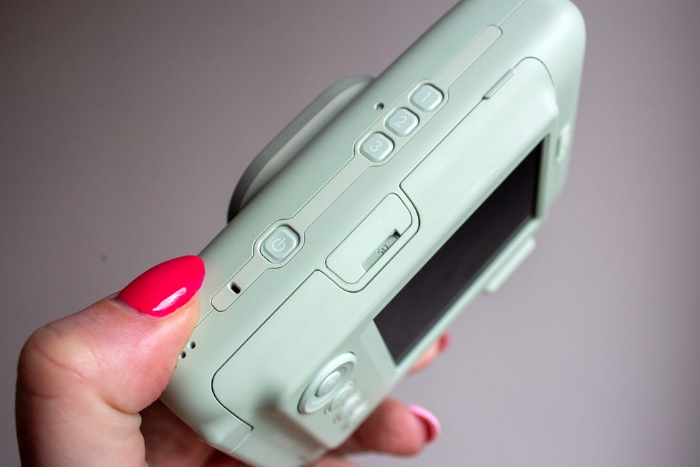 a hand holding a mint green hybrid portable photo printer and instant camera from the side