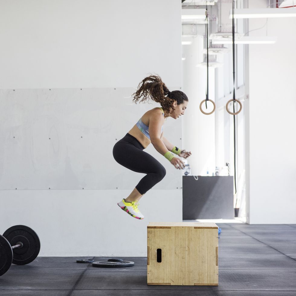 Instructor photographing athlete exercising on jump box in crossfit gym