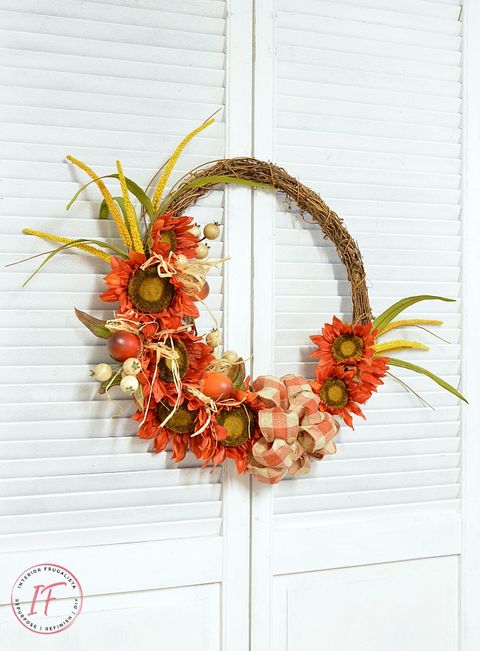 grapevine wreath decorated with faux sunflowers, cornhusks and a plaid orange and white bow