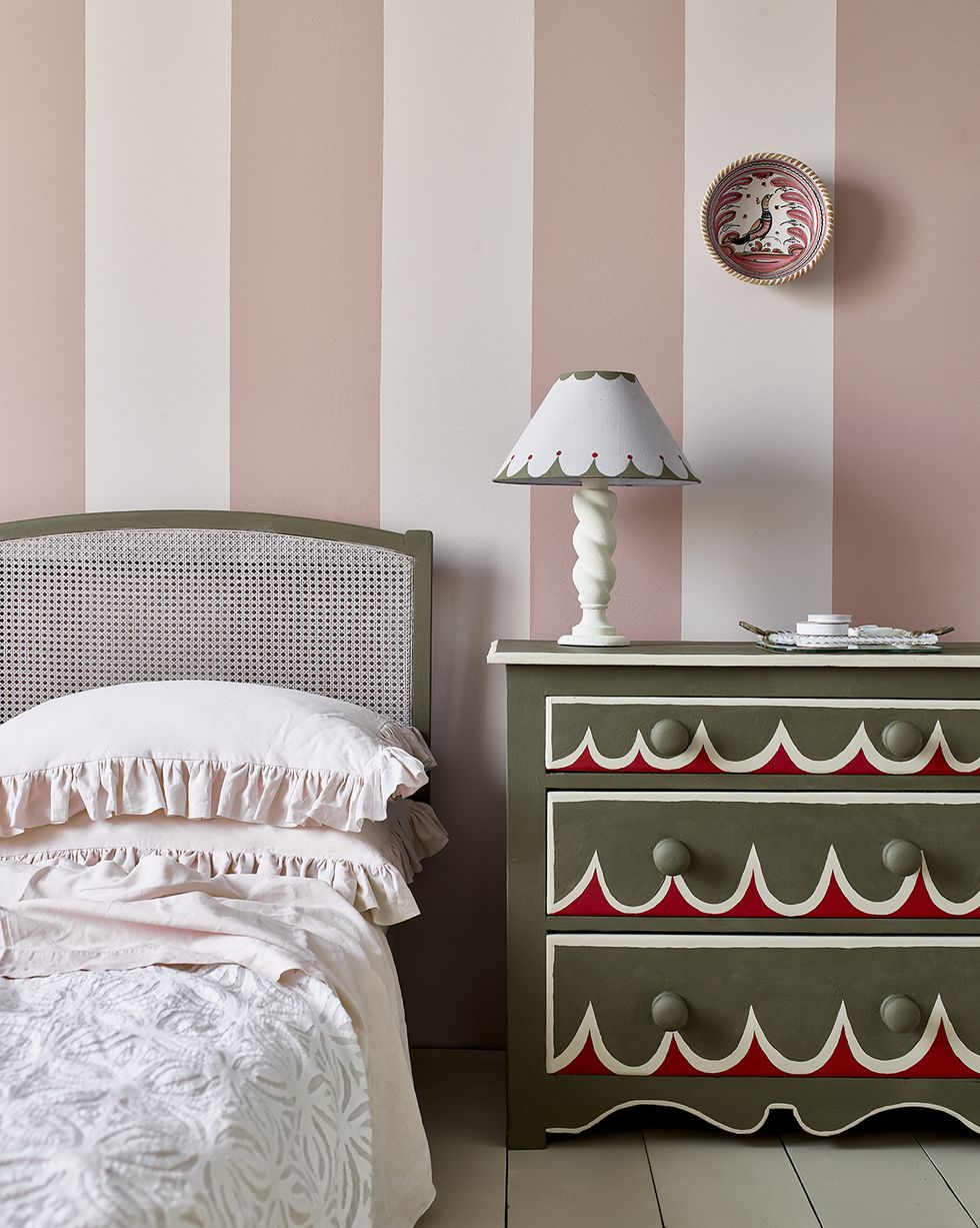 a bed with a lamp on it and a painted chest of drawers