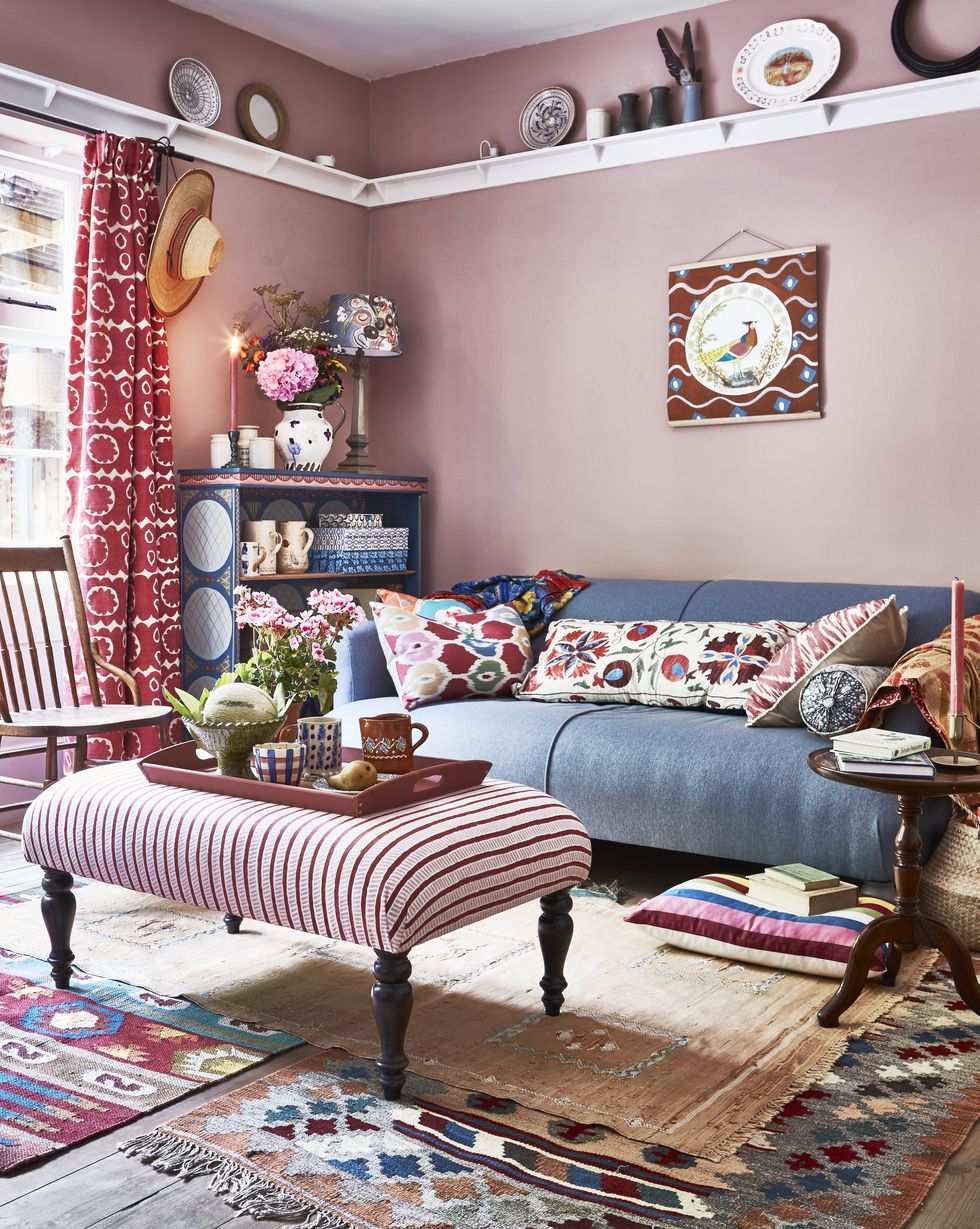 a pink living room with blue sofa, striped footstool and layered rugs
