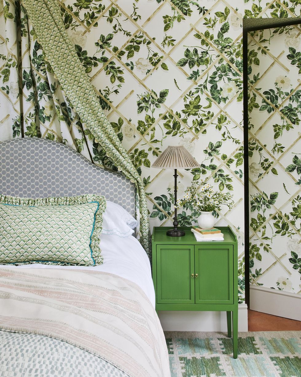 a bedroom with green trellis wallpaper, a bedside table and lamp