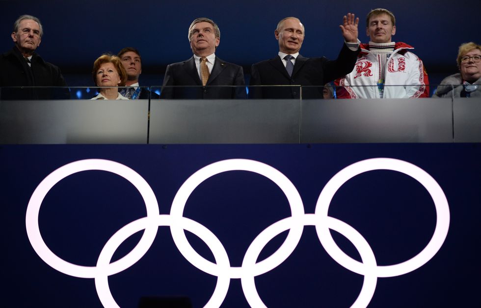vladimir putin waving from a spectator box with the olympic logo below him