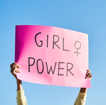 womans hands holding a pink sign reading girl power with the blue sky in the background