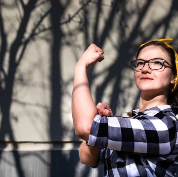 portrait of a young, powerful, beautiful woman wearing glasses and a bandana, flexing her bicep muscle