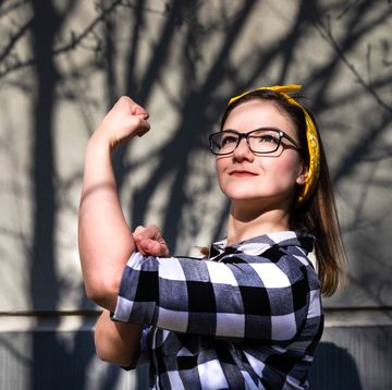 portrait of a young, powerful, beautiful woman wearing glasses and a bandana, flexing her bicep muscle