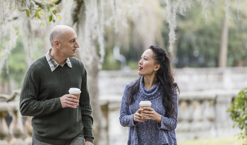 interracial couple walking in park, talking over coffee