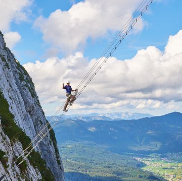 intersport donnerkogel via ferrata in summer, with a man showing a victory sign while climbing the diagonal ladder. stairway to heaven concept.